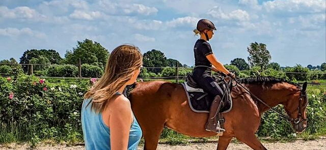 Eine Reitlehrerin unterrichtet eine Reitschülerin auf einem Reitplatz im Sommer