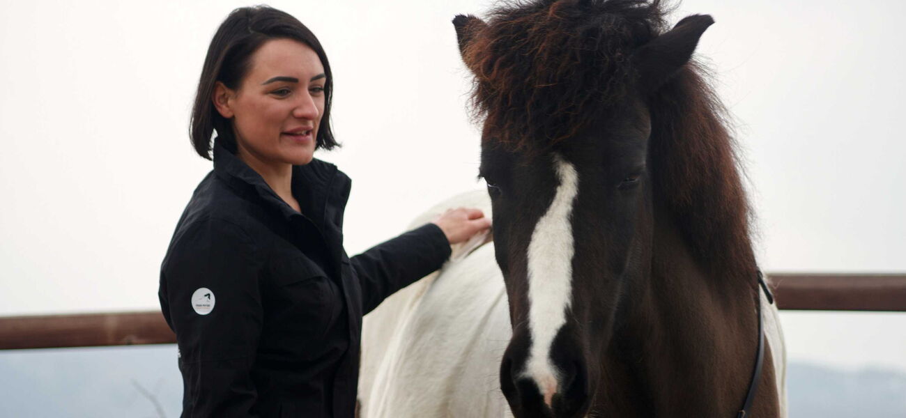 Eine Frau hat eine Hand am Rücken eines gescheckten Ponys und schaut es an