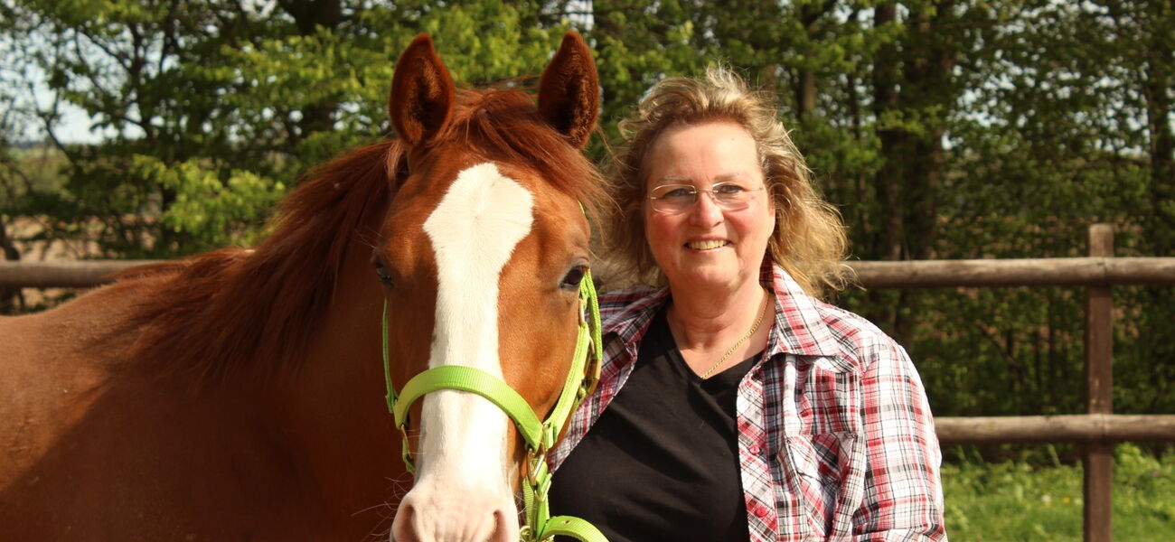 Eine Frau posiert für ein Foto mit einem fuchsfarbenen Pferd und lächelt in die Kamera