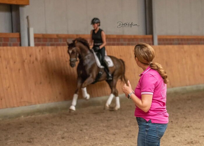 Eine Reitlehrerin unterrichtet eine Reitschülerin auf einem Pferd in der Reithalle